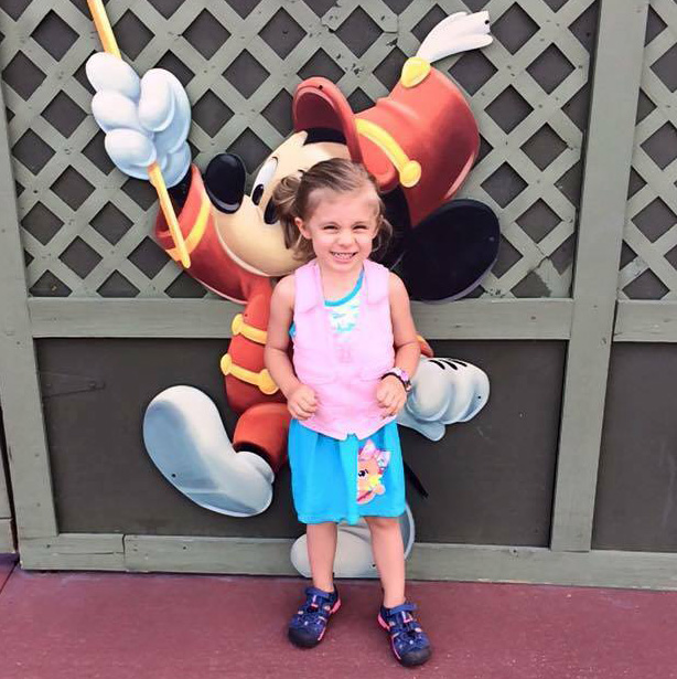 Girl in pink kool max toddler cooling vest standing in front of a picture of Mickey Mouse