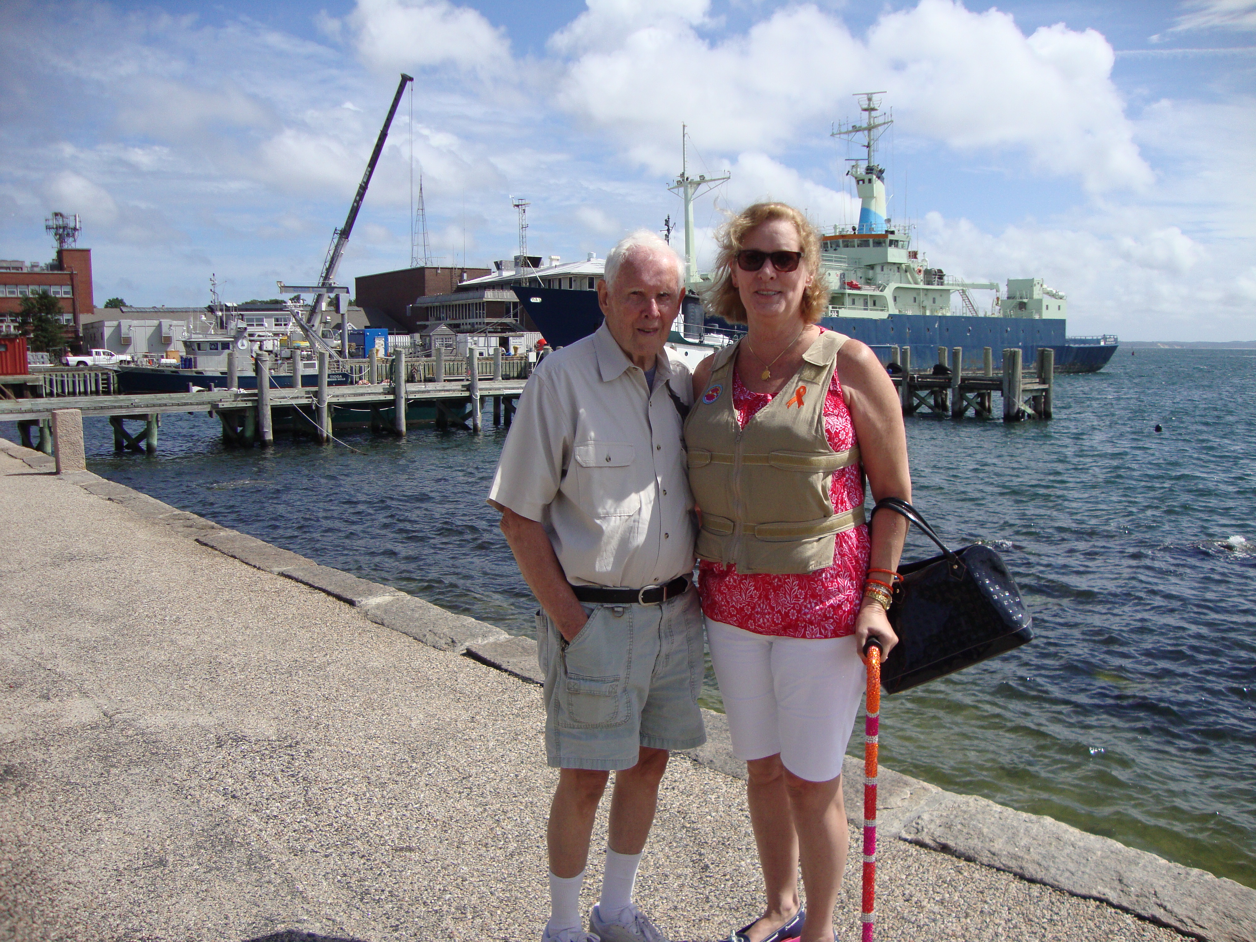 Woman is wearing a khaki Kool Max adjustable zipper front cooling vest standing with a man next to a lake