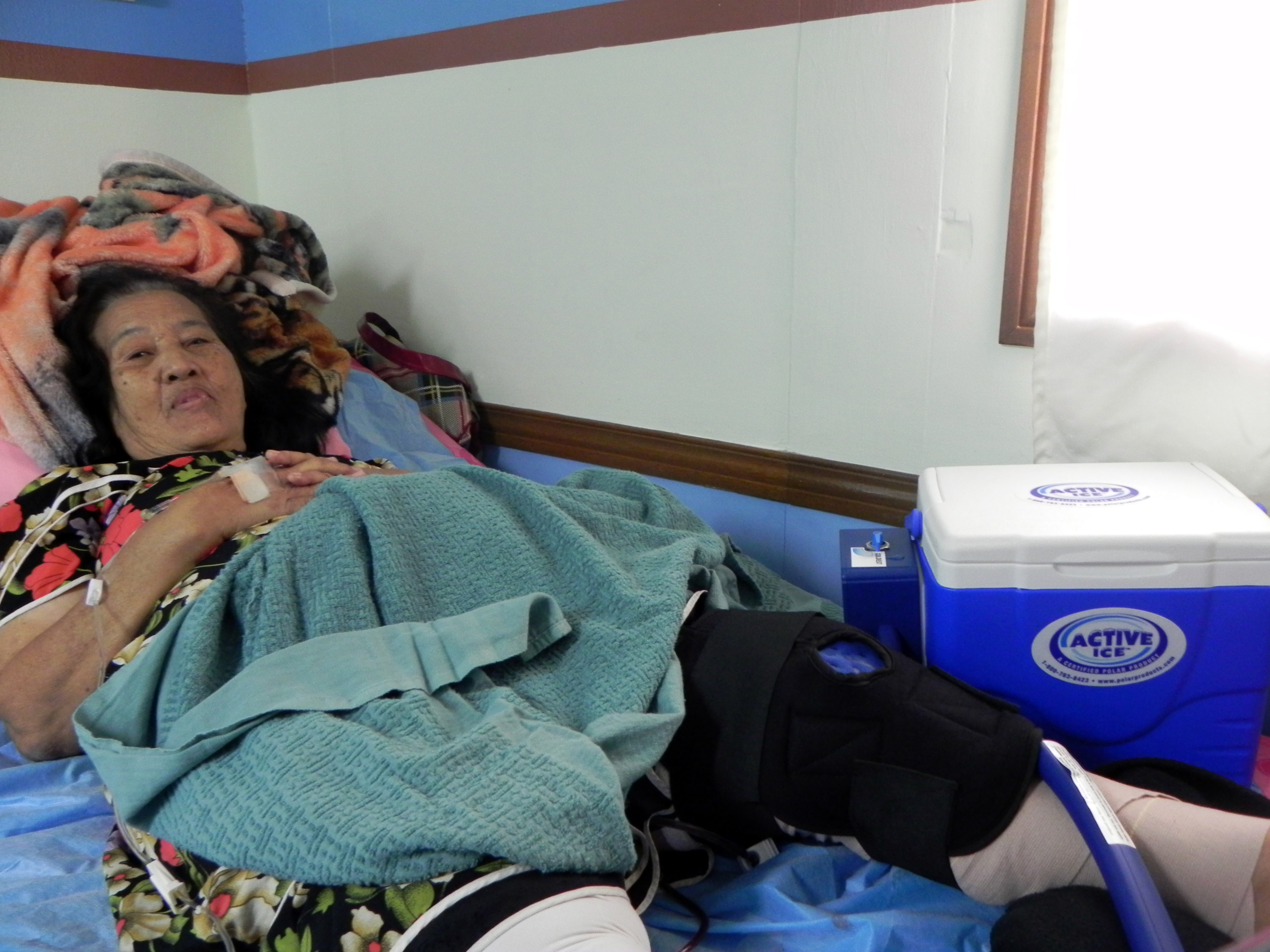 Woman laying in bed using an active ice circulating water therapy system with knee compression wrap on her knee