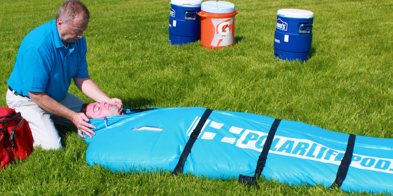 Man in the grass kneeling over a man inside a polar life pod cold water immersion device