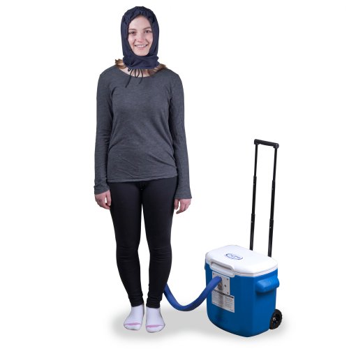 A young woman is standing upright wearing an Active Ice3.0 Cold Water Therapy Head Cap System the Head Cap is connected to the tubing of a 15 quart reservoir the reservoir's handle is fully extended 