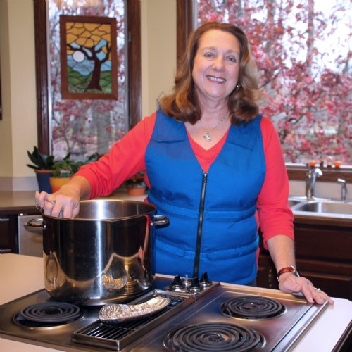 Woman standing in a kitchen over the stove with an Adjustable Cooling Vest on in blue