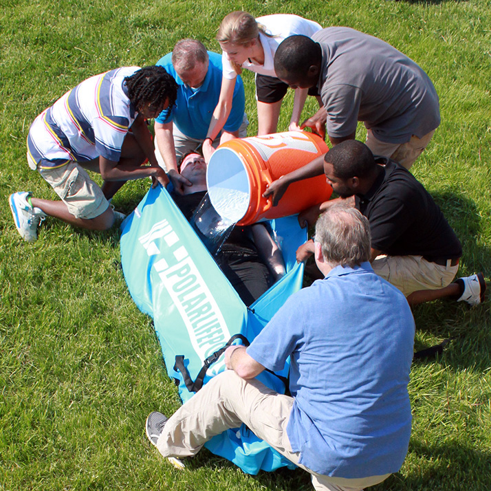 Group of people pouring water on a man in a polar life pod cold water immersion system